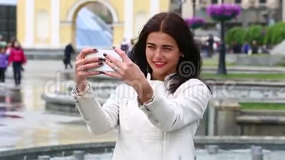 女孩用智能手机笑的肖像在喷泉背景上带着手机的漂亮年轻女人很幸福的女人视频的预览图