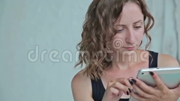 年轻卷曲的女人坐在床上拿着平板电脑多利射击视频的预览图