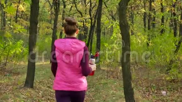 美丽的健身运动女孩穿着运动服穿着运动水瓶或等离子饮料沿着秋天公园散步视频的预览图