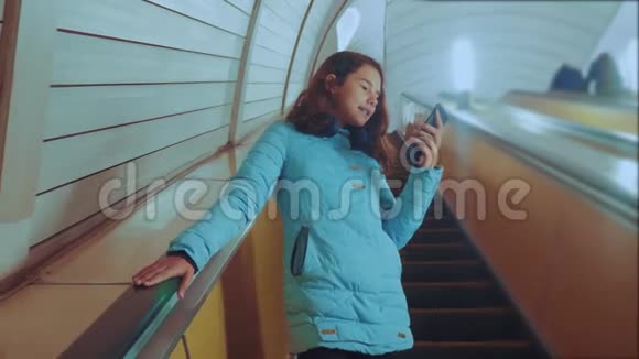 少女生活方式少年在地下地铁乘坐自动扶梯手持智能手机小女孩黑发女儿视频的预览图