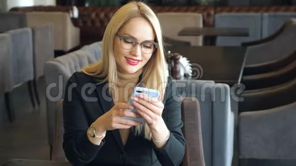 一个金发商务女性穿着西装拿着电话坐在咖啡馆的桌子旁视频的预览图