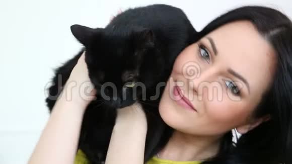 对宠物的爱美丽的黑发女孩带着一只黑猫在家里的沙发上客厅里放松视频的预览图