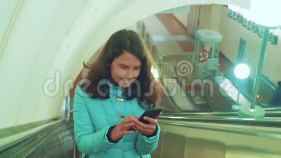 少女在地下地铁乘坐自动扶梯手持智能手机小女孩黑发女儿搜索视频的预览图