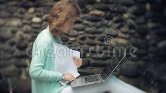 有笔记本电脑和文件的女人在石墙的背景上视频的预览图