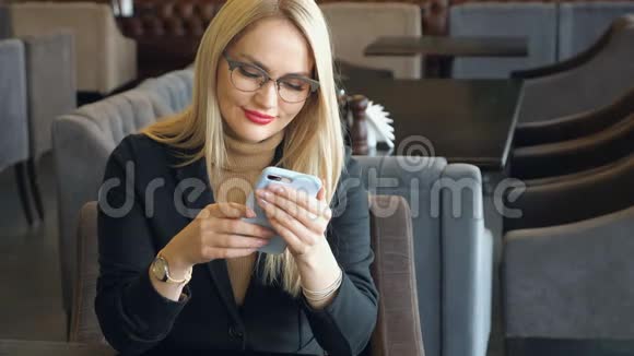 一个金发商务女性穿着西装拿着电话坐在咖啡馆的桌子旁视频的预览图