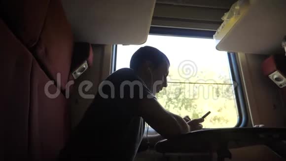 男人的身影坐在火车车厢里坐在窗边坐着一辆智能手机铁路喝酒视频的预览图