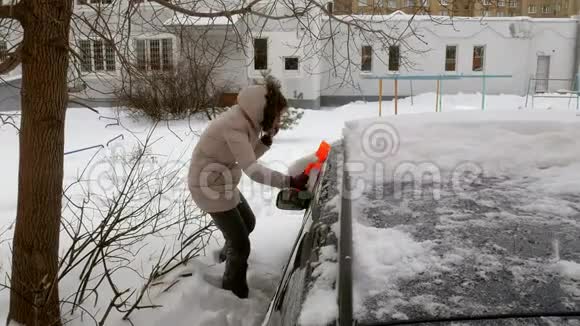 女青年在暴风雪后用刮泥机清洗汽车视频的预览图