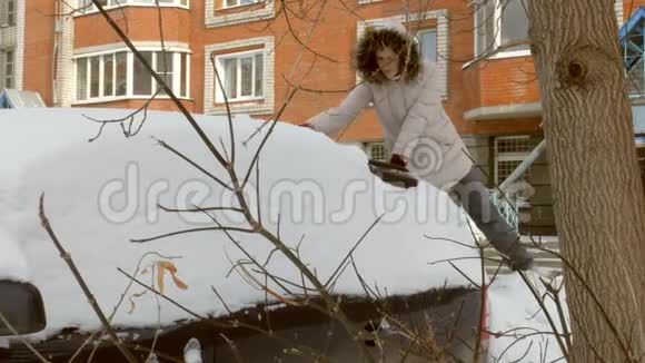 女青年在暴风雪后用刮泥机清洗汽车视频的预览图