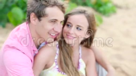 在爱中微笑年轻情侣在沙滩上坐着拥抱视频的预览图