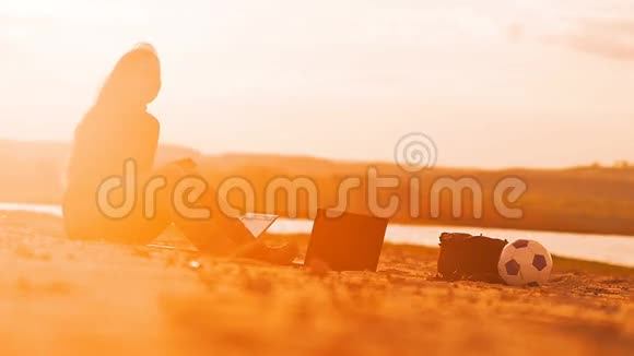 他坐在沙滩上拿着笔记本电脑女孩慢动作视频视频的预览图