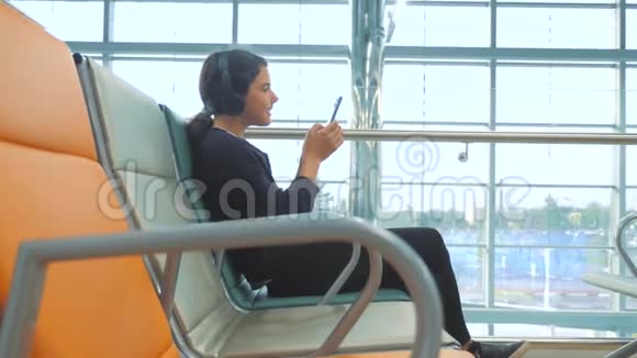 机场候机大厅供飞机飞行年轻快乐的少女戴着生活方式耳机听音乐视频的预览图