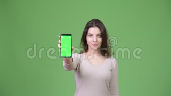 年轻快乐的美女在绿色背景下展示电话视频的预览图