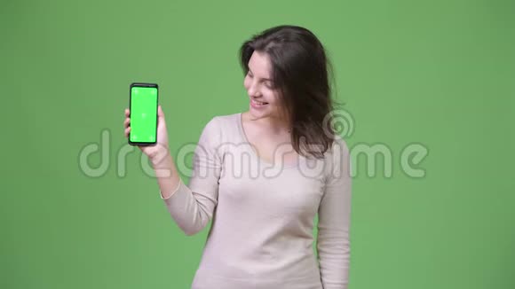 年轻快乐的美女在绿色背景下展示电话视频的预览图