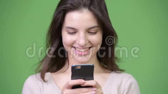 年轻快乐的美女微笑着用绿色背景的手机视频的预览图