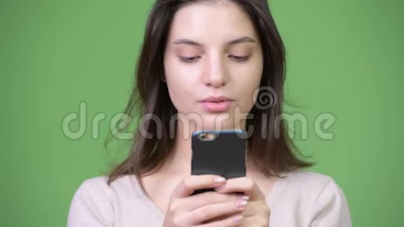 年轻的美女在绿色背景下使用手机视频的预览图