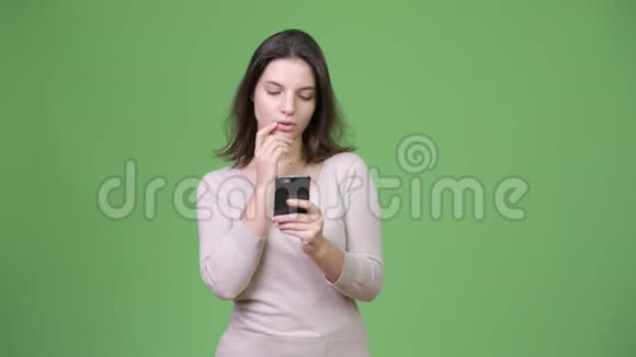 年轻快乐的美女在绿色背景下用电话思考视频的预览图