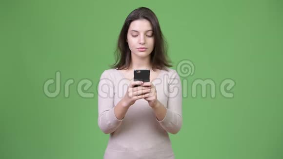 年轻的美女在绿色背景下使用手机视频的预览图