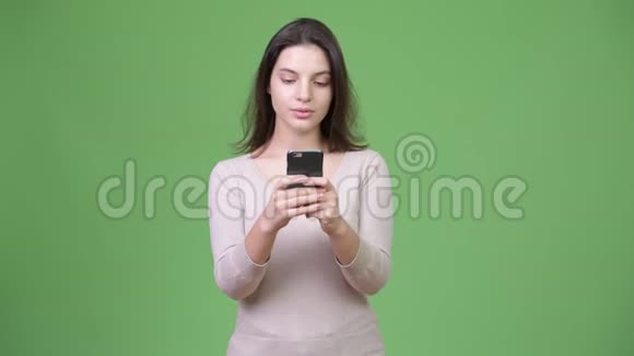 年轻的美女在绿色背景下使用电话思考视频的预览图