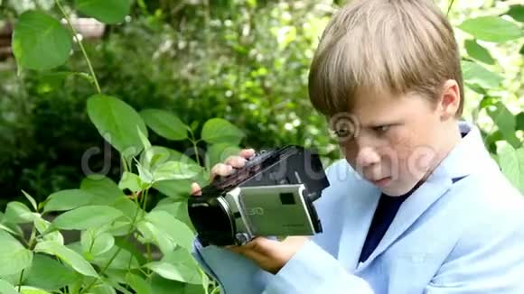 年轻的男孩带着摄像机拍摄关于绿色公园背景的自然视频的预览图