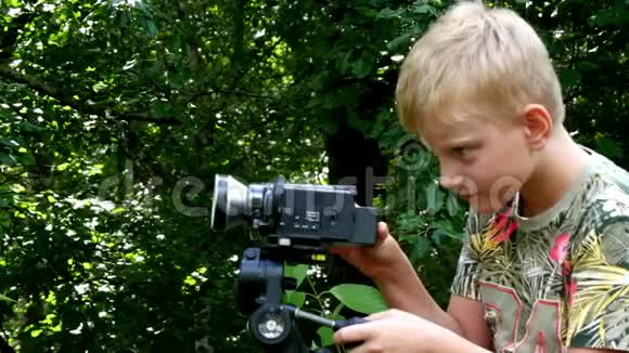 年轻的男孩带着摄像机拍摄关于绿色公园背景的自然视频的预览图