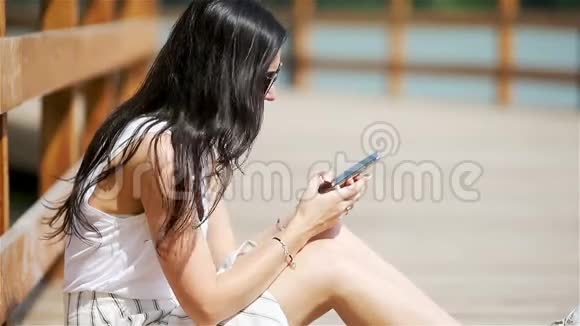 可爱的女人坐在公园里一边用手机看短信视频的预览图