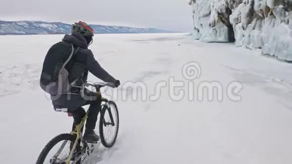 人正骑自行车在冰窟附近有冰洞和冰柱的岩石非常美丽骑自行车的人穿着视频的预览图