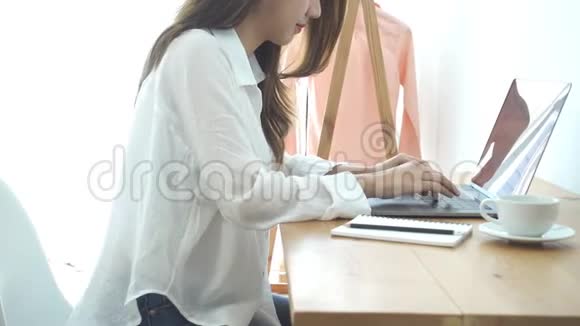 美丽的年轻微笑的女人在笔记本电脑上工作一边享受着温暖的咖啡坐在家里的客厅里视频的预览图