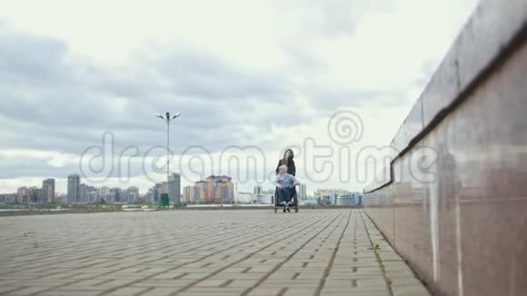 坐轮椅的残疾人和年轻女子在城市大街上散步视频的预览图