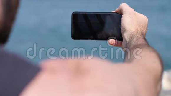 年轻人用手机在海滩拍照视频的预览图