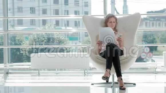 漂亮的女商人坐在玻璃办公室的白色椅子上检查文件视频的预览图