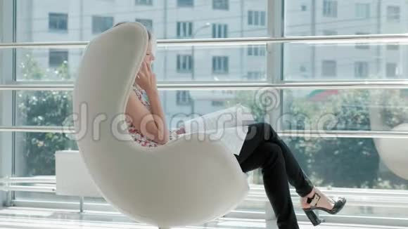 漂亮的商人坐在玻璃办公室的白色椅子上检查文件视频的预览图