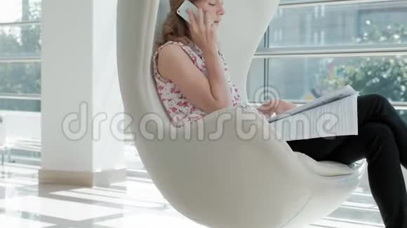 漂亮的商人坐在玻璃办公室的白色椅子上检查文件视频的预览图