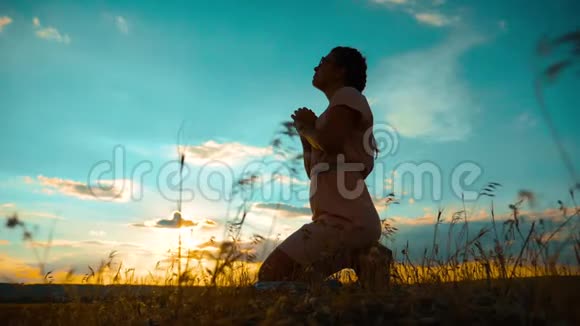 女孩在日落时双手交叉祈祷剪影慢动作视频女孩双手交叉祈祷祈求上帝视频的预览图