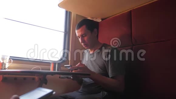 男人坐在火车车厢里拿着一部生活方式的智能手机喝着咖啡和茶慢动作视频的预览图