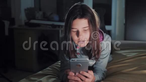 十几岁的女孩网上购物在床上看智能手机一个少女写的生活方式视频的预览图