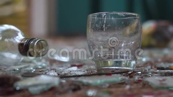 碎玻璃背景上的一杯伏特加掉落的瓶子视频的预览图