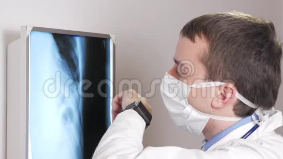 一位戴面膜的年轻医生在诊所里使用一只智能手表这个人告诉病人x光结果视频的预览图