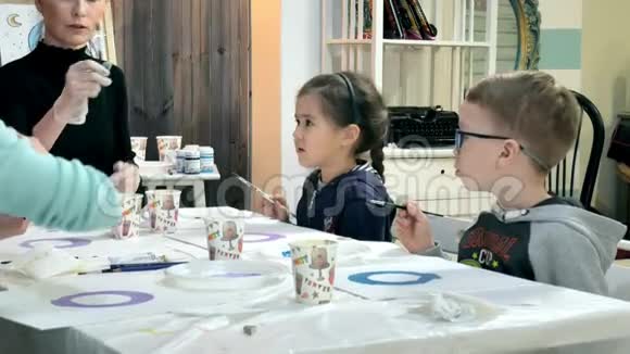 孩子们男孩和女孩在教室里围着桌子坐在一起画画与他们在一起的是他们的年轻视频的预览图