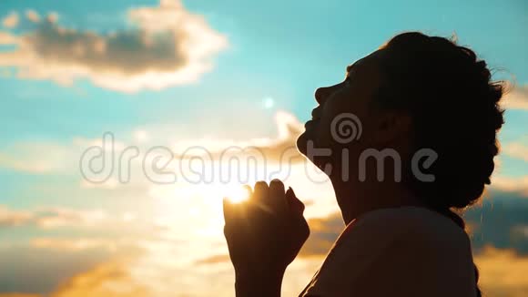 女孩在祈祷女孩在日落时交叉双手祈祷剪影慢动作视频女孩的生活方式让她双手合拢视频的预览图