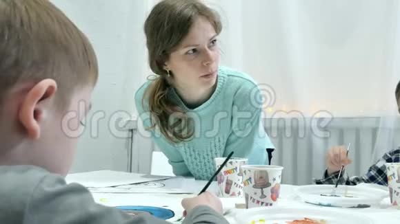 孩子们在教室里围着桌子坐在一起画画和他们在一起的是他们年轻美丽的老师视频的预览图