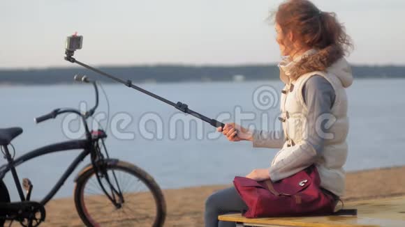 美丽的女孩微笑着用智能手机在河岸上自拍视频的预览图