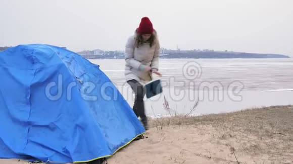 迷人的年轻旅游妇女戴着红帽子在海岸森林附近收集一个旅游帐篷视频的预览图