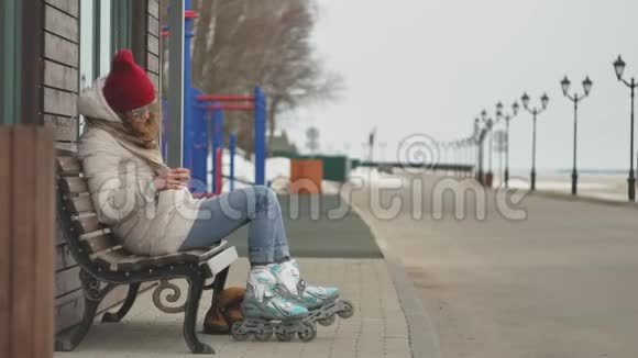 年轻漂亮的女人戴着红帽子穿着运动温暖的衣服和滚筒坐在木凳上喝茶视频的预览图