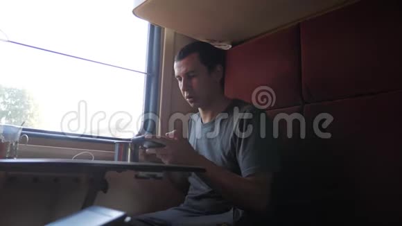 男人坐在火车上坐在铁路车厢里拿着智能手机喝着咖啡和茶慢动作视频的预览图