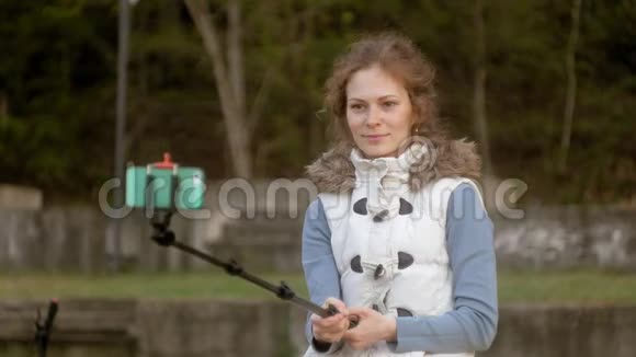 漂亮女孩微笑着用智能手机在公园里自拍视频的预览图
