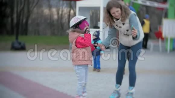妈妈和女儿骑着溜冰鞋女孩学习溜冰摔倒妈妈教女儿骑车视频的预览图
