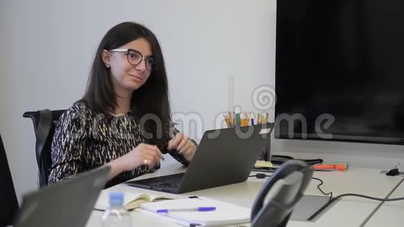 年轻女子坐在桌子旁现代办公室里拿着笔记本电脑视频的预览图