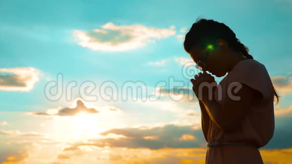 女孩在日落时双手交叉祈祷剪影慢动作视频女孩双手交叉祈祷祈求上帝视频的预览图