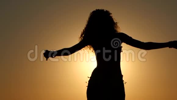 女孩在海滩上跳舞在夕阳下跳舞剪影式视频的预览图