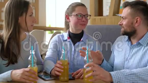 三个朋友坐在咖啡馆里喝果汁在交流中玩得开心视频的预览图
